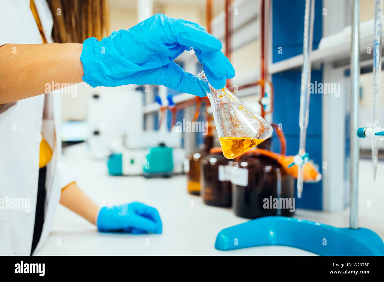 La donna o mani femminili in guanti protettivi tenere il tubo di prova nelle mani di chimica produce esperimento di test e la ricerca in un moderno laboratorio di chimica. Foto Stock