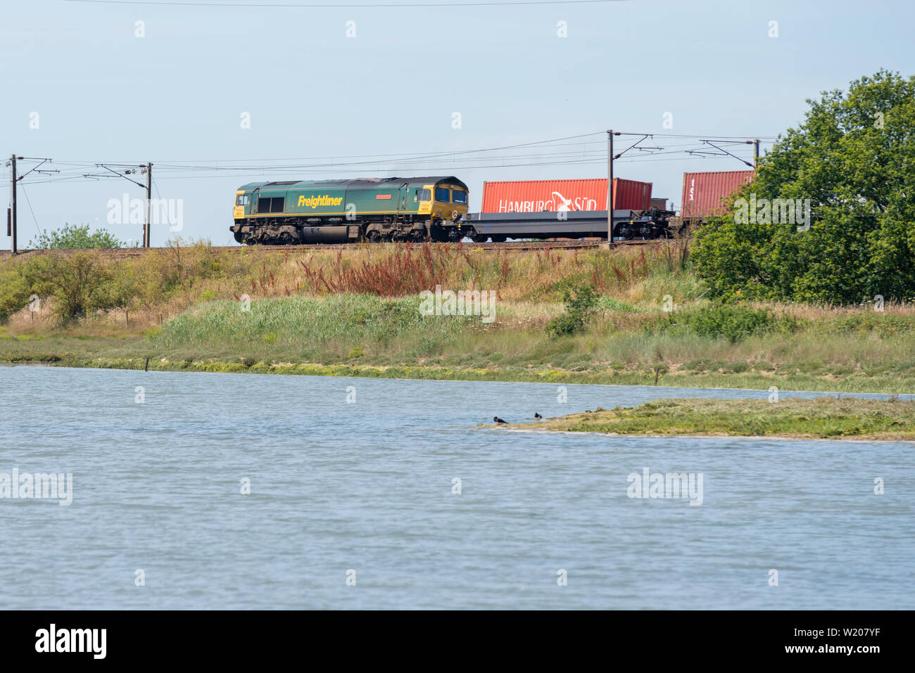 Freightliner Classe 66 diesel locomotiva elettrica trasporta un treno merci sulla costa est la linea di maggiore Anglia stazione ferroviaria nei pressi di Manningtree, Essex Foto Stock