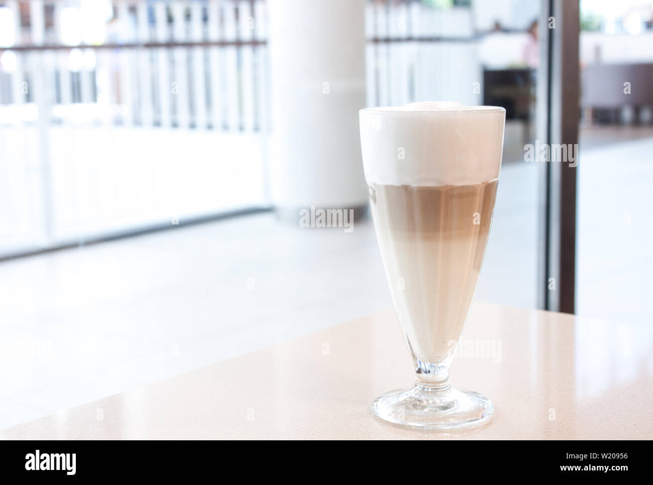 Caffè Latte in vetro con grande tall schiuma bianca in bianco e arredamento moderno, nel centro commerciale per lo shopping. Foto Stock