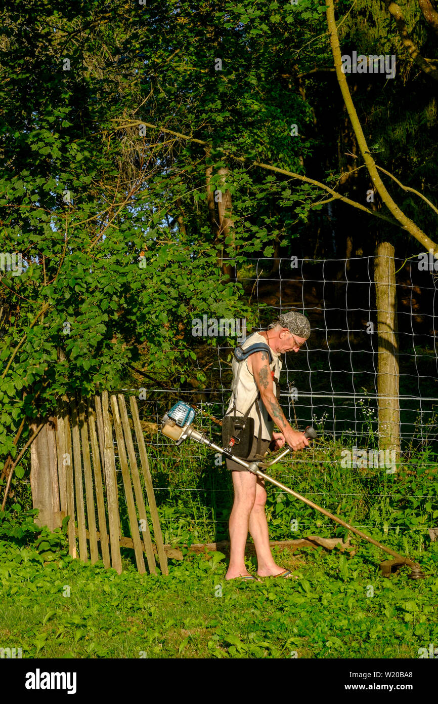 Uomo che utilizza un decespugliatore per tagliare erba e piante infestanti in un giardino Zala county Ungheria Foto Stock