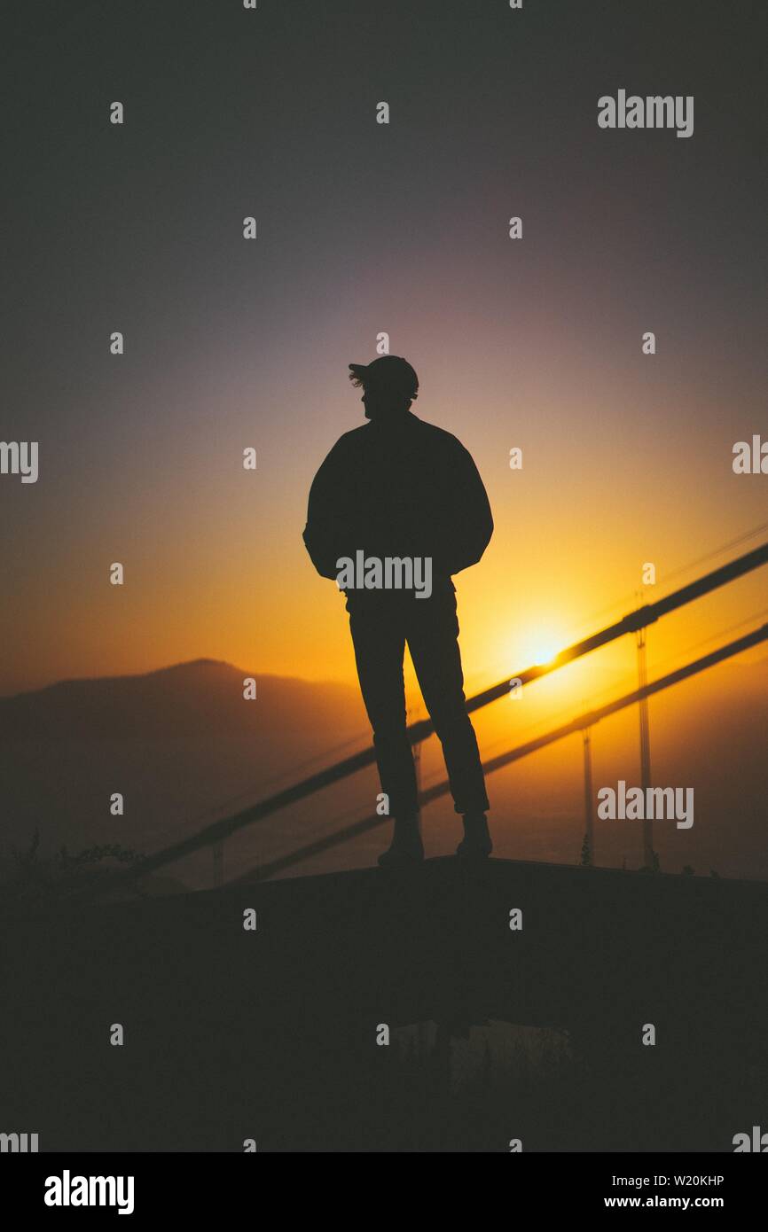 Silhouette di un giovane maschio in piedi sulla scala dietro scale con splendida vista del tramonto Foto Stock