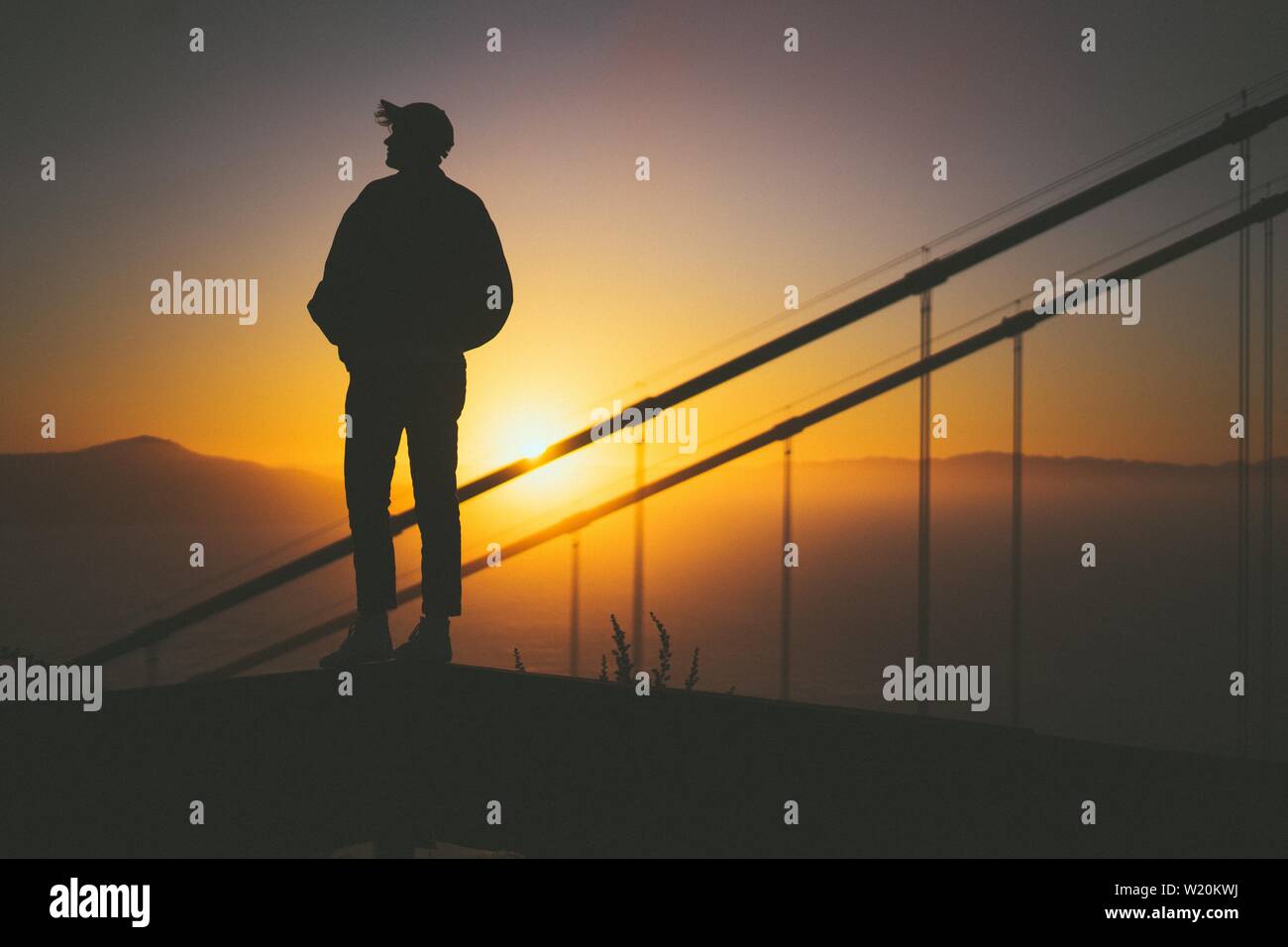Silhouette di un giovane maschio in piedi sulla scala dietro scale con splendida vista del tramonto Foto Stock