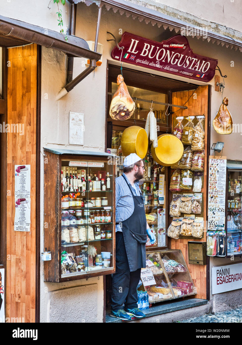 Fornitore locale attende i clienti all'ingresso della loro attività nel borgo di Orta San Giulio nel Lago d'Orta durante un pomeriggio estivo Foto Stock