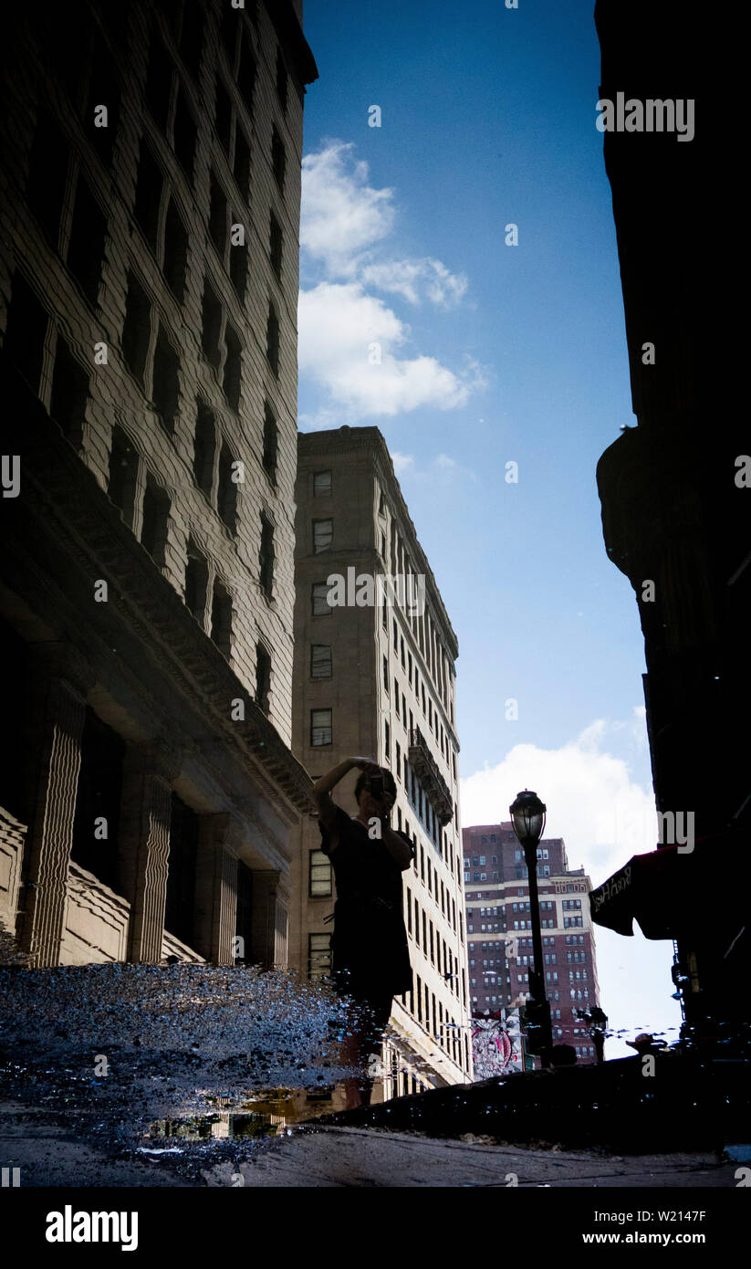 La riflessione di una donna in una pozza d'acqua sulla strada nel centro di Philadelphia Foto Stock
