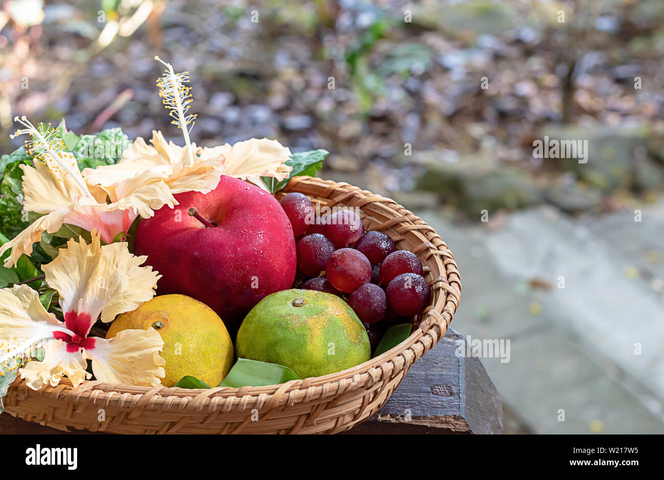 Mela, arancio e uva in armatura cestelli di bambù con decorazioni floreali lo sfondo sfocato alberi. Foto Stock