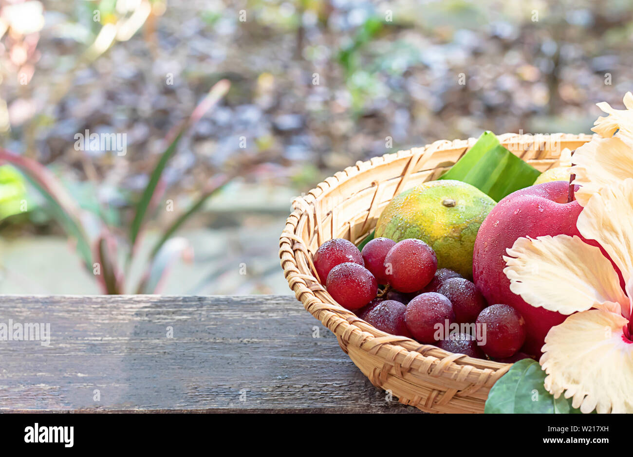 Mela, arancio e uva in armatura cestelli di bambù con decorazioni floreali lo sfondo sfocato alberi. Foto Stock
