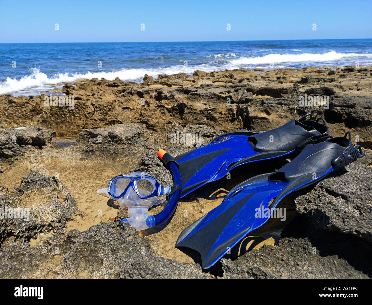 Blue pinne e maschera per lo snorkeling e le immersioni giacciono sulla riva del mare con onde e cielo blu su sfondo Foto Stock