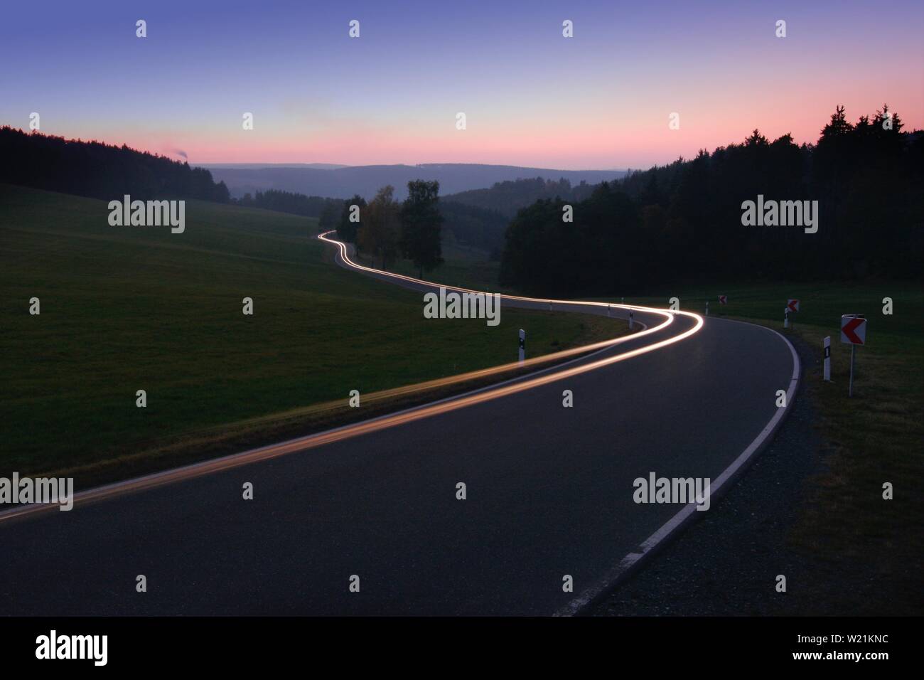 Guida auto sul paese di avvolgimento strada in serata, luce bianca tracce, vicino a Bad Lobenstein, Turingia, Germania Foto Stock