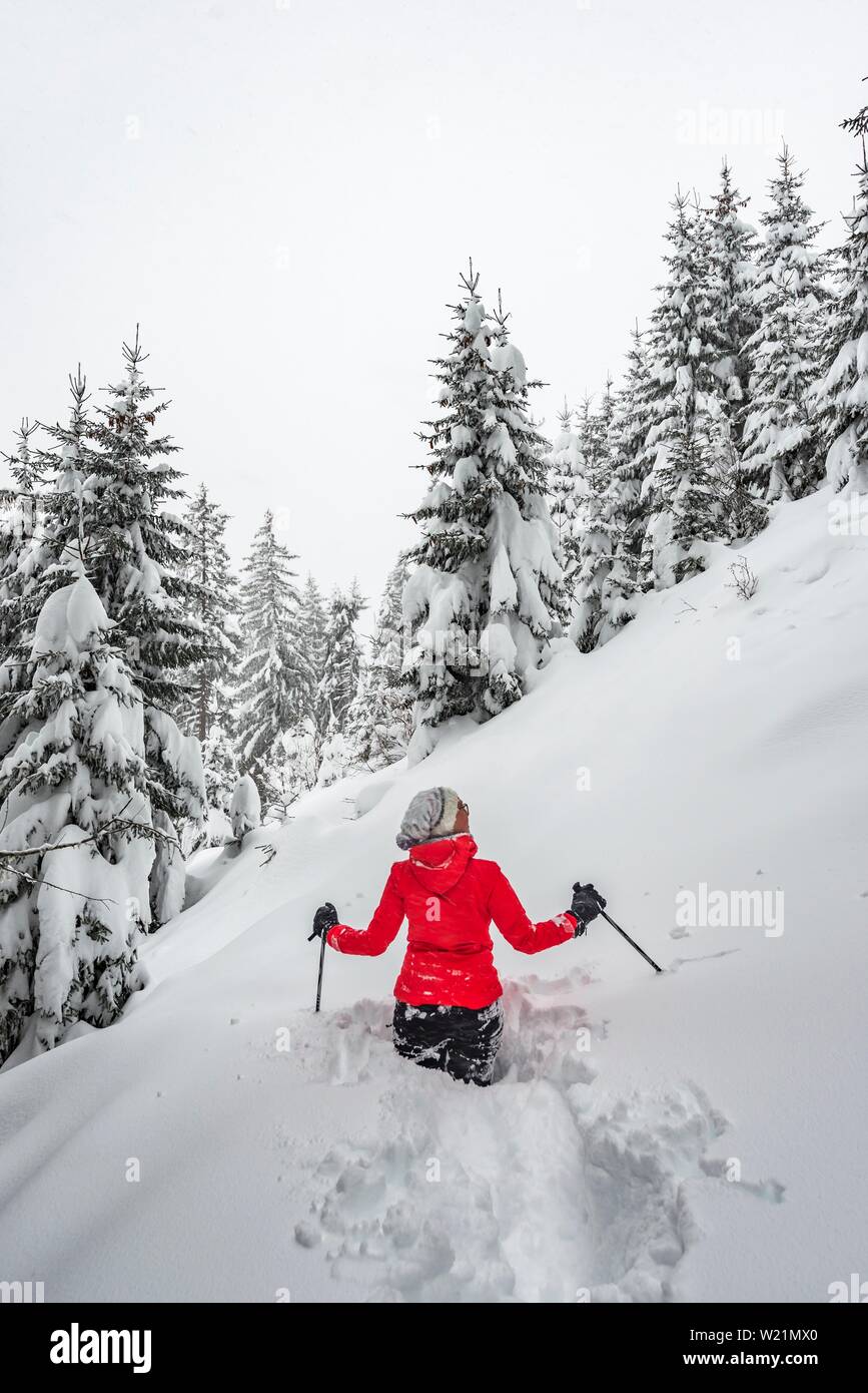 Giovane donna in piedi nella neve profonda, escursionismo in inverno, neve profonda nella foresta, Brixen im Thale, Tirolo, Austria Foto Stock