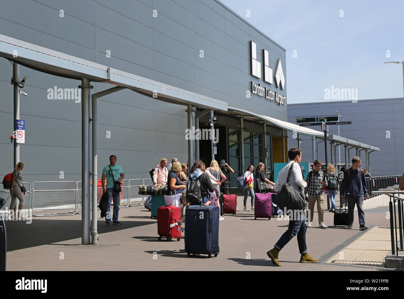 L'aeroporto London Luton, Regno Unito. I passeggeri con bagaglio approccio l'ingresso del nuovo edificio del terminal. Mostra il nuovo logo airport sopra. Foto Stock