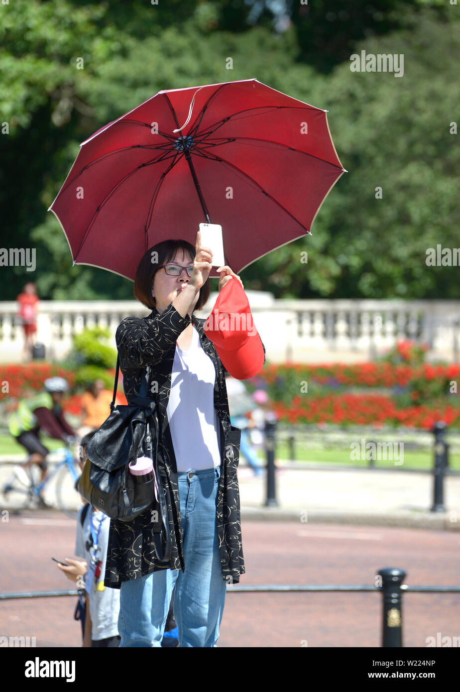 Londra, Inghilterra, Regno Unito. Asian turistico con un ombrello in una calda giornata di sole di scattare una foto con il suo telefono cellulare Foto Stock