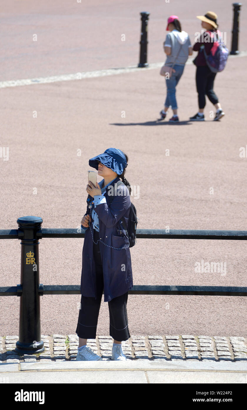 Londra, Inghilterra, Regno Unito. Giovane donna giapponese che indossa un cappotto in una giornata molto calda Foto Stock