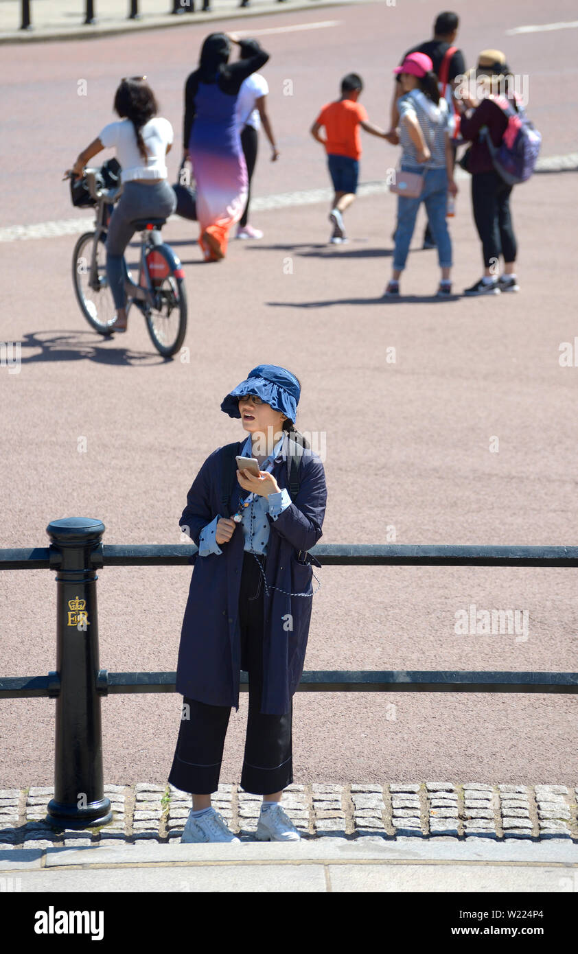 Londra, Inghilterra, Regno Unito. Giovane donna giapponese che indossa un cappotto e cappello in una giornata molto calda Foto Stock