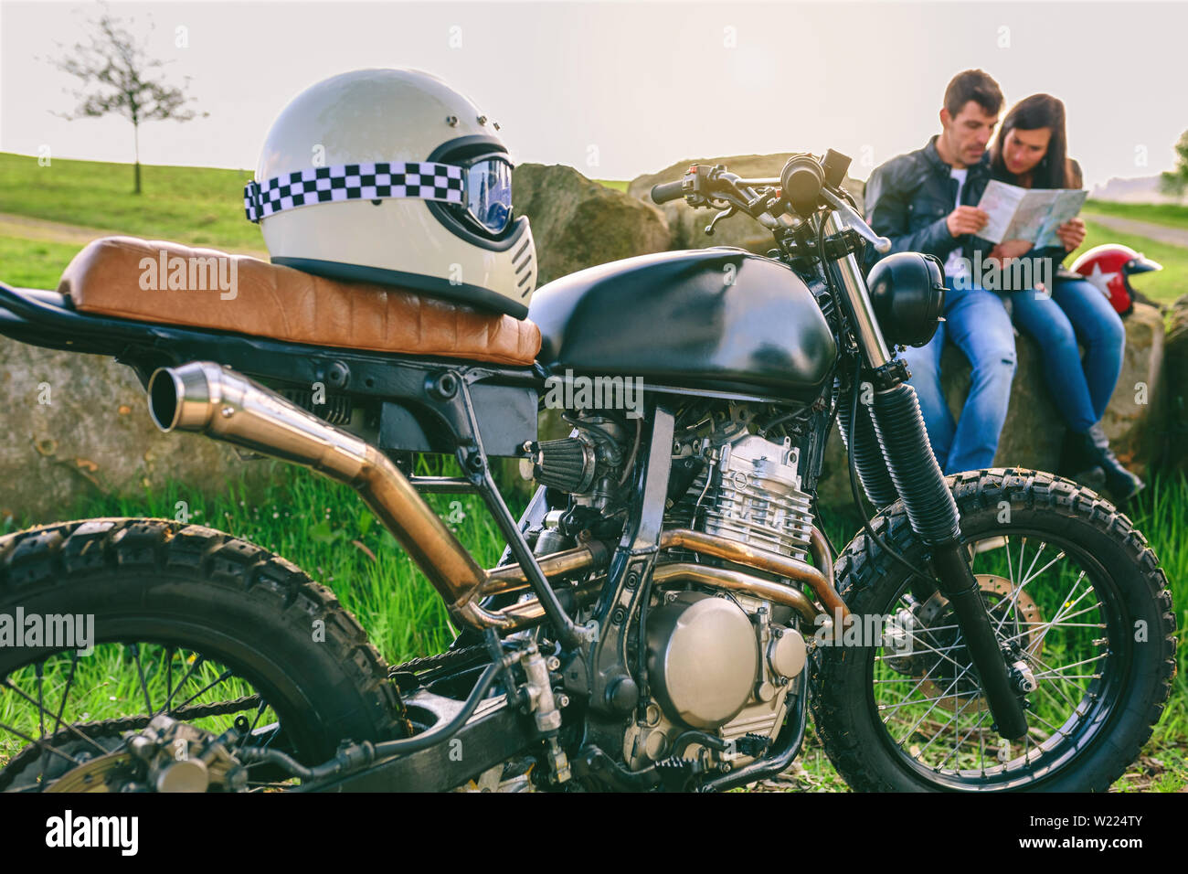 Motocicletta personalizzata con il casco e la giovane coppia in cerca di una mappa Foto Stock