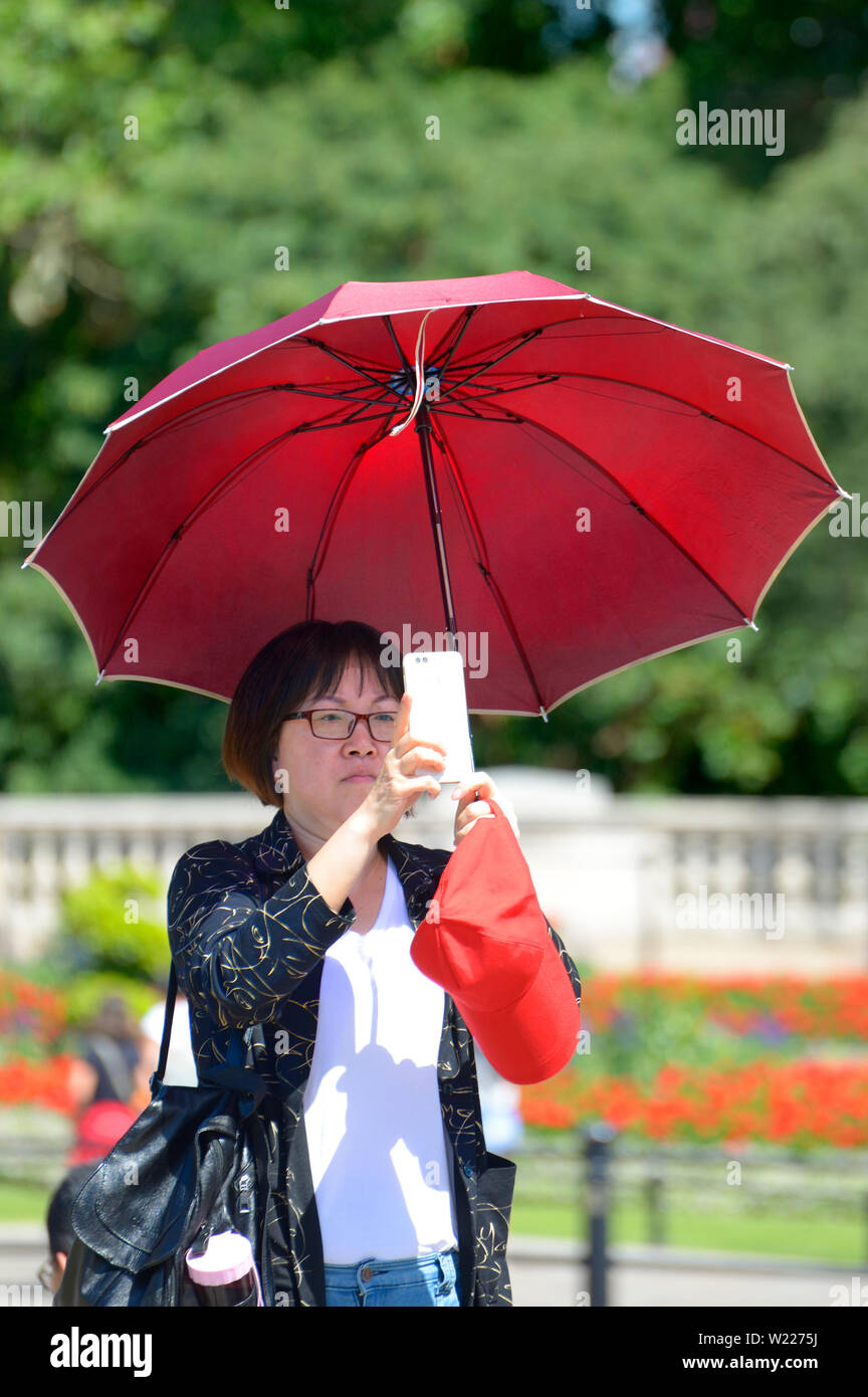 Londra, Inghilterra, Regno Unito. Asian turistico con un umbreaal su una calda giornata di sole di scattare una foto con il suo telefono cellulare Foto Stock