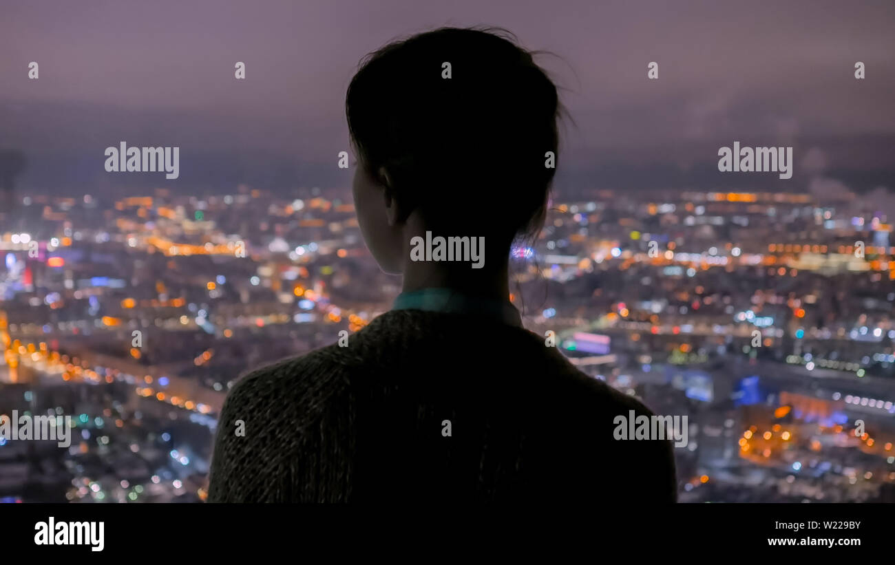 Malinconici donna che guarda la città di notte dal grattacielo Foto Stock