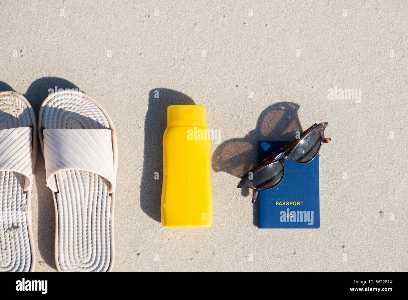 Riposo in spiaggia: pantofole, crema protettiva e occhiali da sole sulla sabbia pulita. Accessori per vacanze al mare o le vacanze estive e passaporto biometrico Foto Stock
