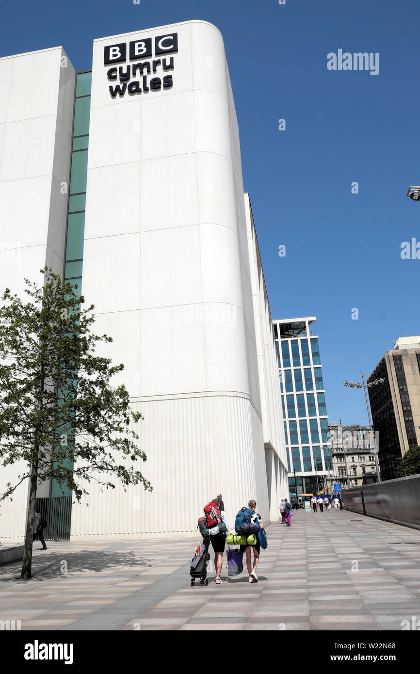 Giovani con zaini a piedi dalla stazione ferroviaria passato la nuova BBC Cymru Wales edificio nella piazza centrale di city centre Cardiff Wales UK KATHY Foto Stock