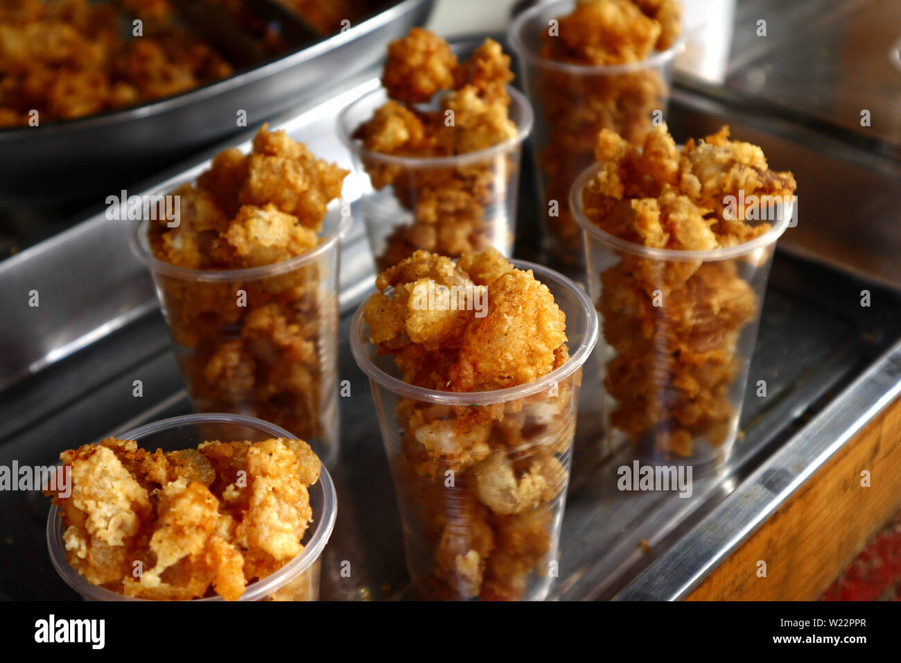 Foto di profondo fritto di pollo pelle venduti presso un chiosco di cibo su un marciapiede lungo una strada trafficata. Foto Stock