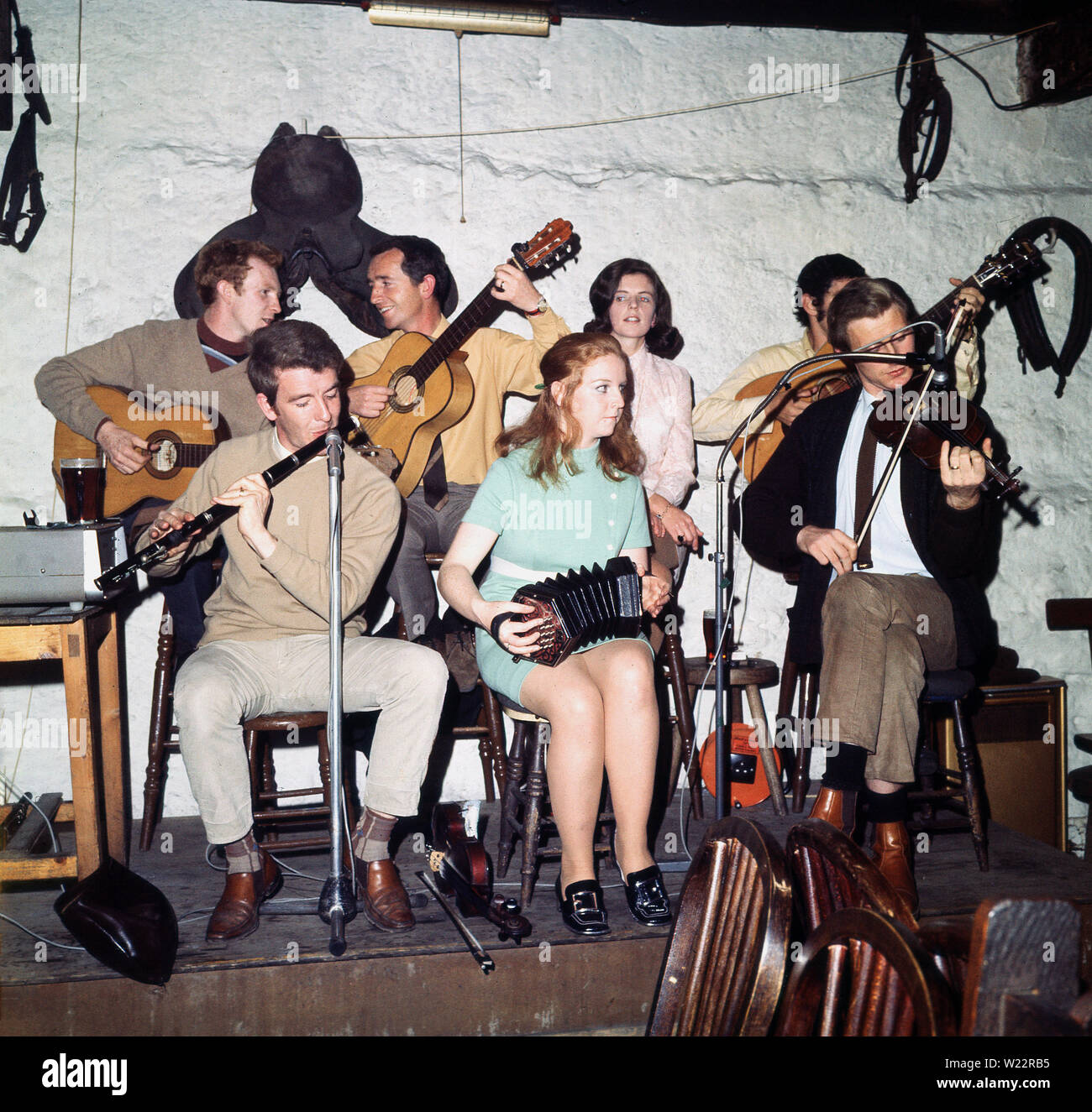 1960, storico, un gruppo di musicisti che suonano insieme seduti su sgabelli su un piccolo palco di legno in un pub di Dublino, Dublino, Irlanda. La musica tradizionale irlandese presenta una varietà di strumenti musicali, come si può vedere qui - il flauto, il violino, le chitarre - ed è un elemento importante del patrimonio e della cultura irlandese, in particolare..... avendo il pazzo, il divertimento. Foto Stock