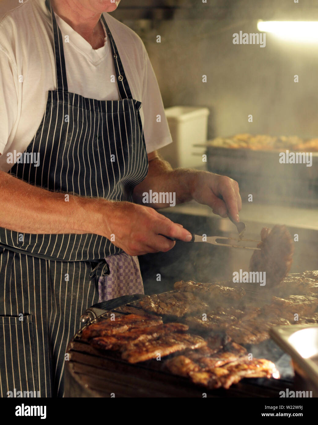 Uomo che indossa un grembiule lavorando la griglia per il barbecue Foto  stock - Alamy
