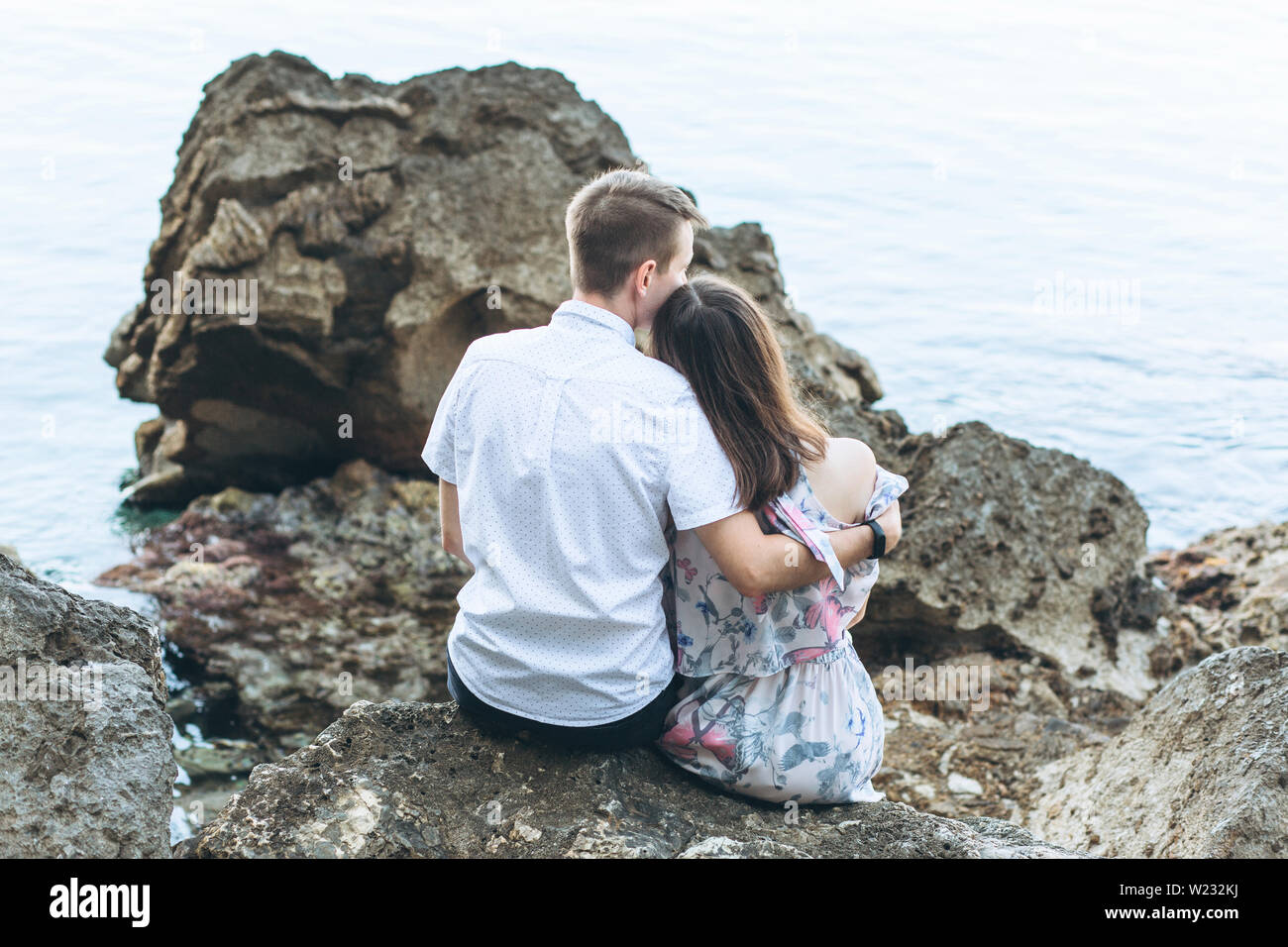Un irriconoscibile coppia giovane siede sulla costa e ammira il mare. Egli abbraccia il suo. Foto Stock