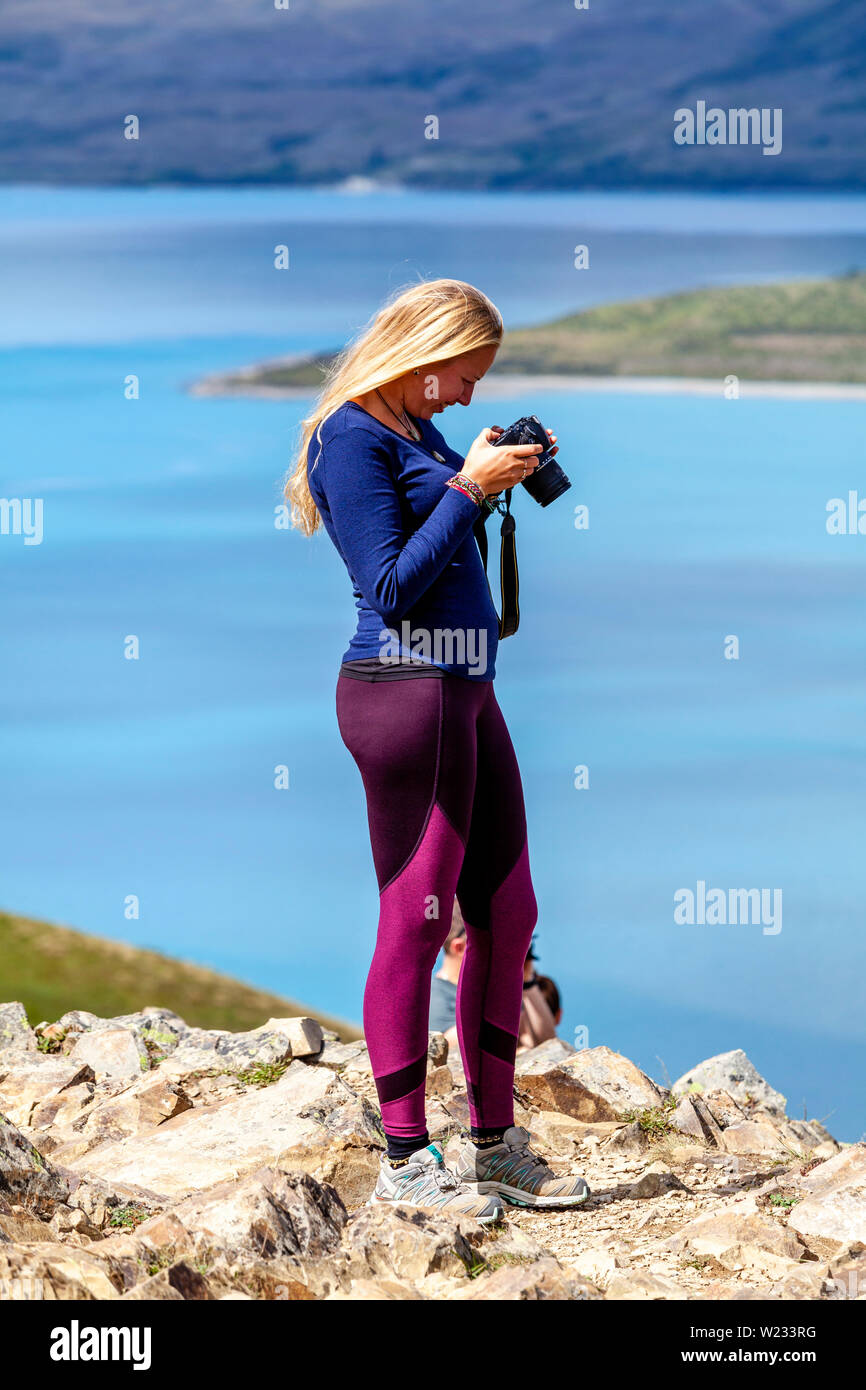 Giovane donna guardando le foto sul suo telefono, Lago Tekapo, Isola del Sud, Nuova Zelanda Foto Stock