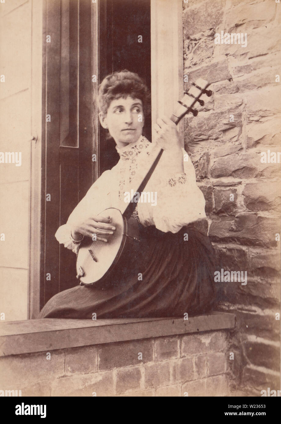 Victorian fine 1880 / inizio 1890 fotografia di una donna seduta su una parete d'ingresso a "Raglan House', Borth, Galles suonare il banjo ukulele. Foto Stock