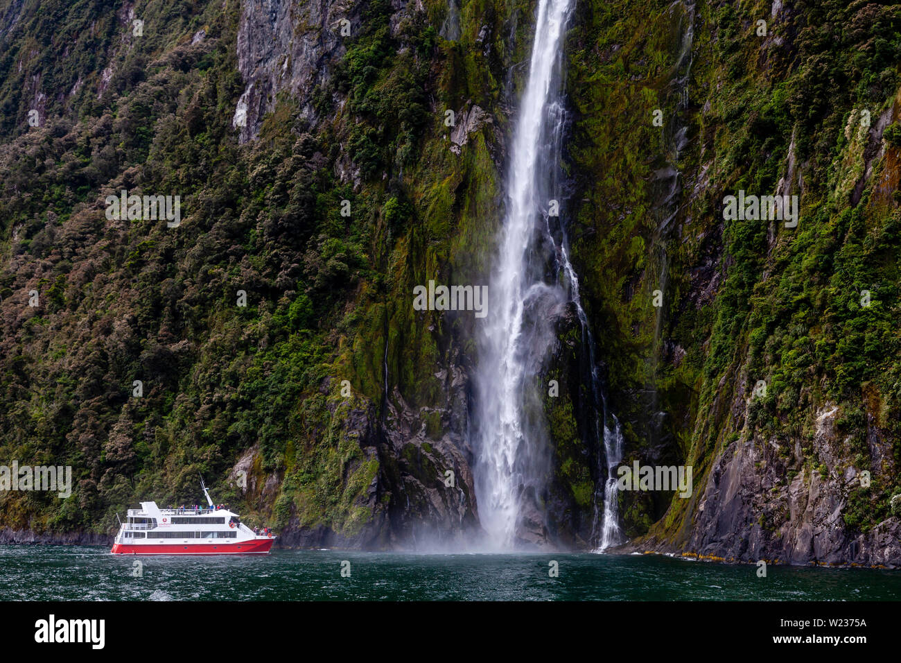 A Milford Sound barca si avvicina una cascata, il Parco Nazionale di Fiordland, Isola del Sud, Nuova Zelanda Foto Stock