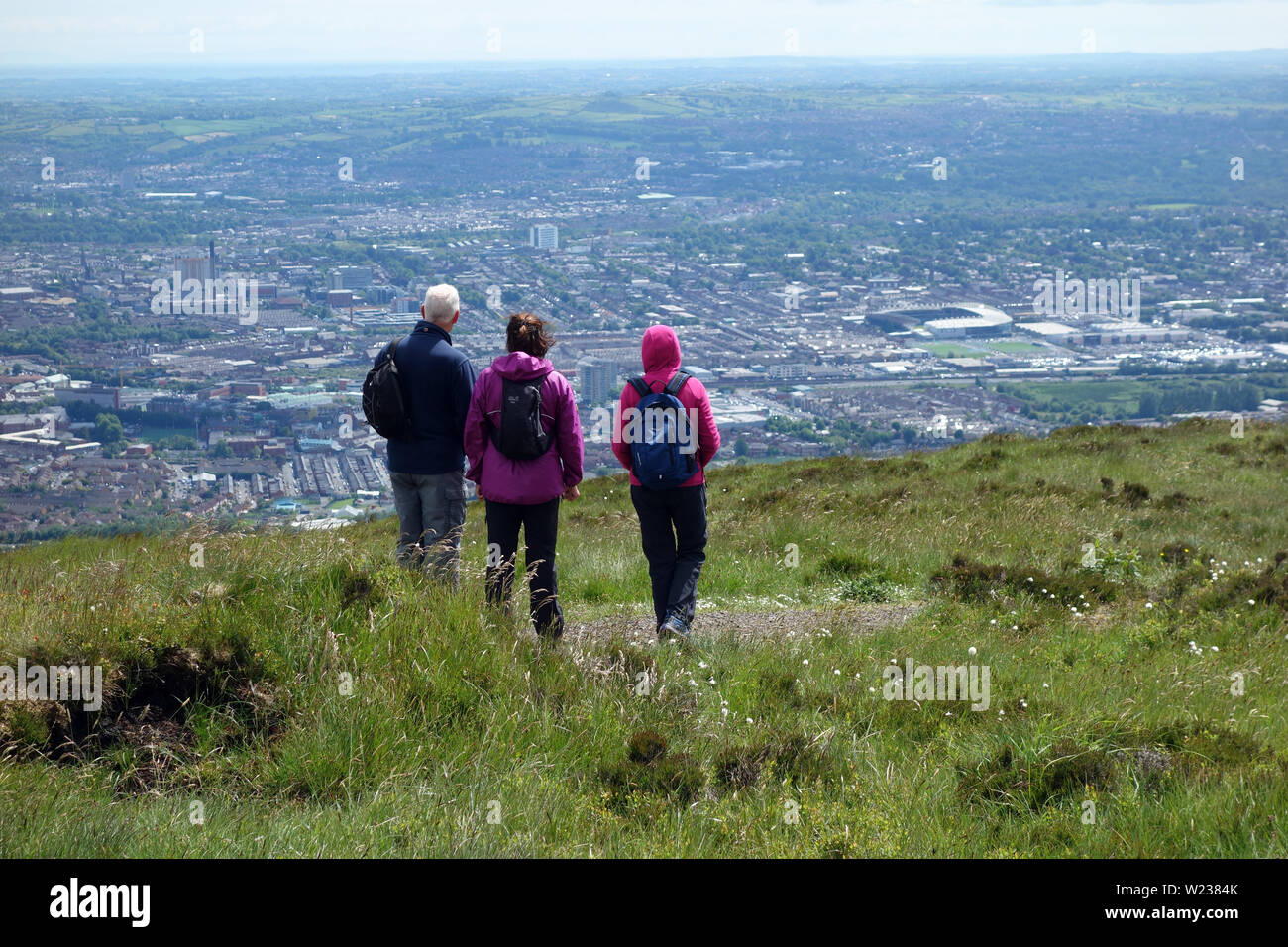Tre i camminatori guardando verso il basso sulla città di Belfast dalla Montagna Nera Ridge Trail nella contea di Antrim, Irlanda del Nord, Regno Unito. Foto Stock