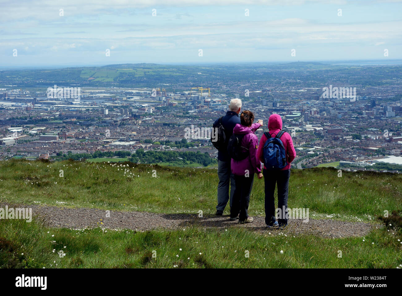 Tre i camminatori guardando verso il basso sulla città di Belfast dalla Montagna Nera Ridge Trail nella contea di Antrim, Irlanda del Nord, Regno Unito. Foto Stock