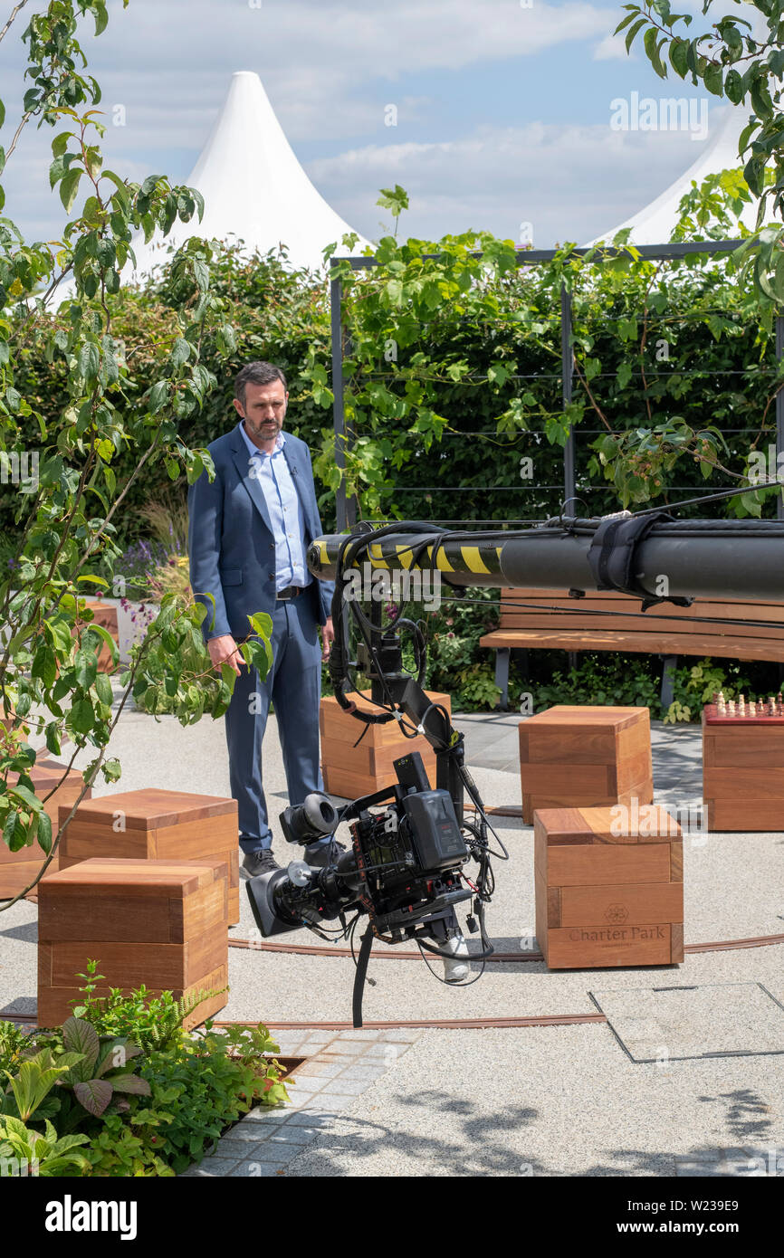 Adam Frost facendo un pezzo di telecamera in uno spettacolo giardino alla RHS Hampton Court flower show 2019. Hampton Court Palace, Surrey, Regno Unito Foto Stock