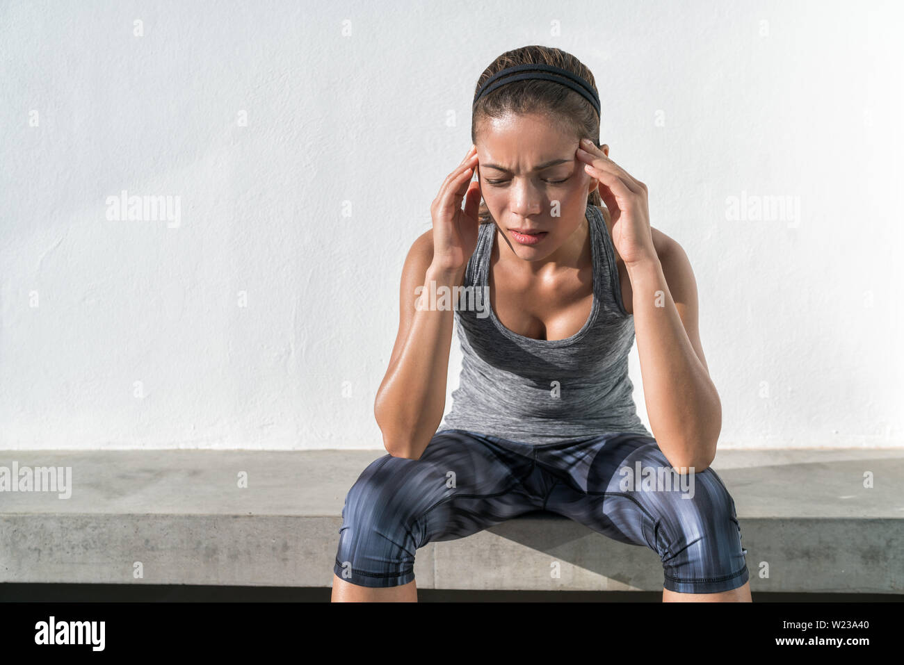 Atleta in funzione fitness donna con mal di testa emicrania dolore durante l'allenamento cardio run. Atleta asiatico con il problema della salute sensazione di esaurimento durante il difficile allenamento di forza esercizio in palestra. Foto Stock