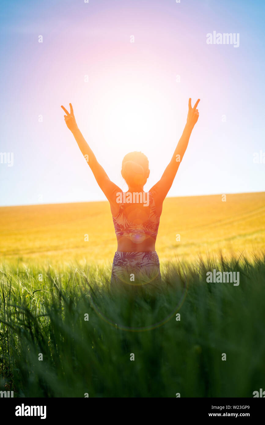 Vista posteriore di una donna ad alba con le braccia sollevate in gioia e libertà in piedi in un campo di grano Foto Stock