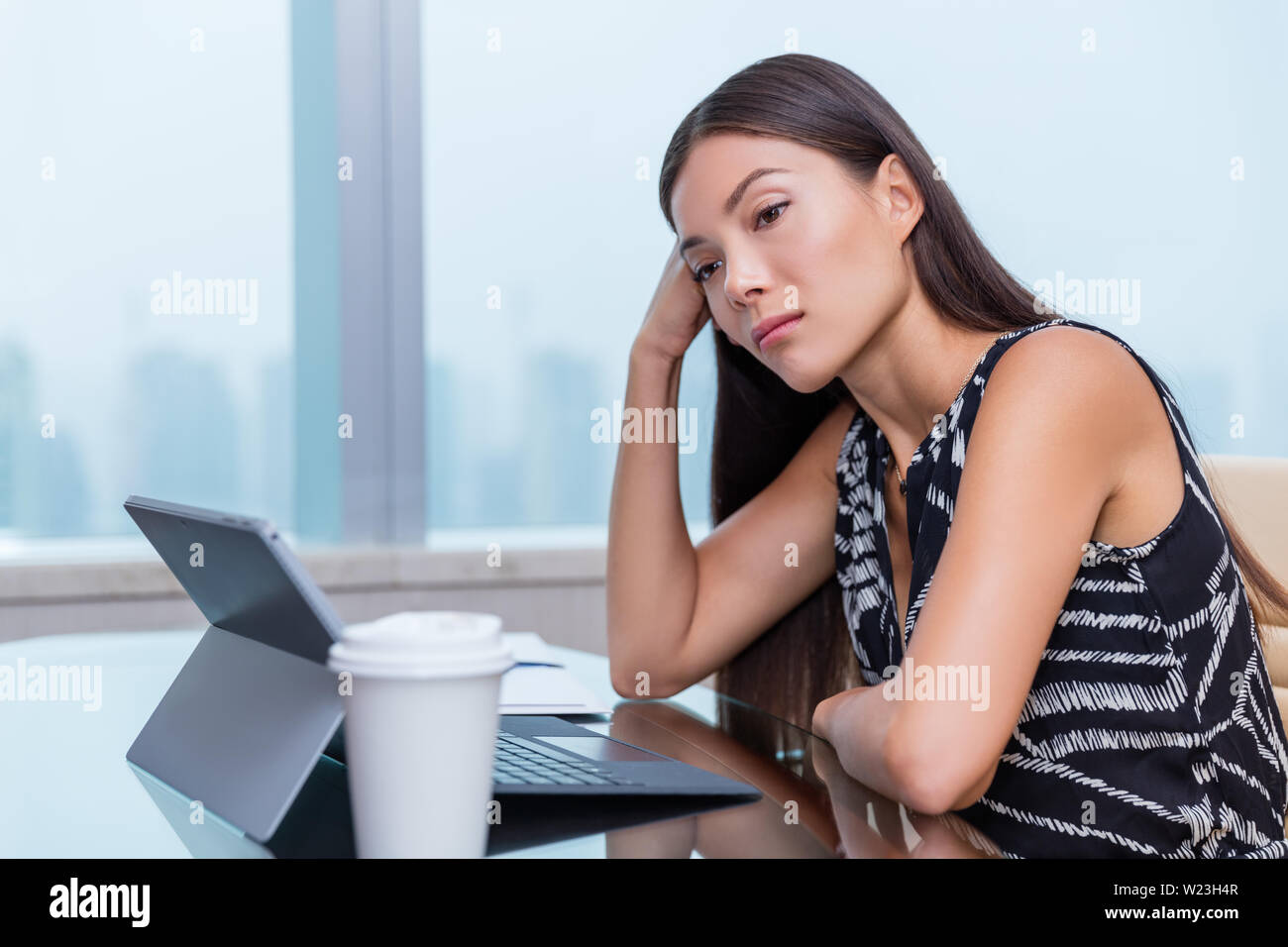 Annoiato o triste donna che lavorano in ufficio lavoro. Negativo il concetto di lavoro. Stanco imprenditrice seduto alla scrivania nella parte anteriore del computer portatile a pensare a problemi e mostrare insoddisfazione di carriera. Foto Stock