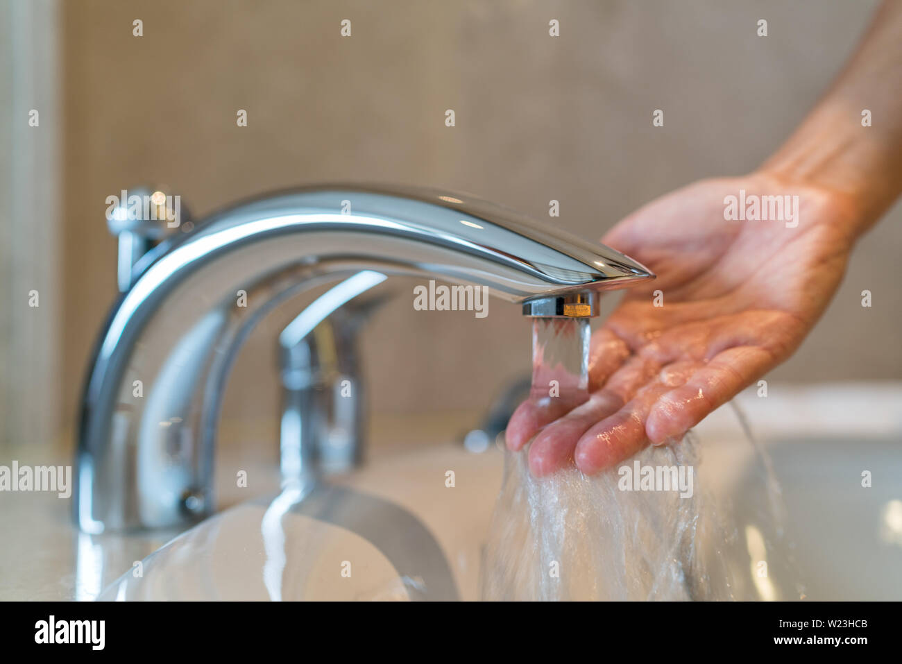 Donna di prendere un bagno a casa controllare temperatura toccare acqua corrente con la mano. Primo piano sulle dita sotto acqua calda al di fuori di un rubinetto di un lavandino o vasca nel bagno della casa Foto Stock