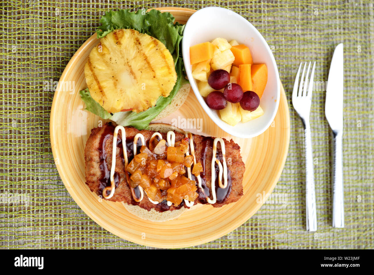 Hawaiian giapponese cibo fusion, Hawaii cultura. Piastra ristorante closeup di karaage hamburger di pollo, giapponese fritto di pollo specialità con chutney, mayonnais, grigliate di ananas e frutta fresca lato. Foto Stock