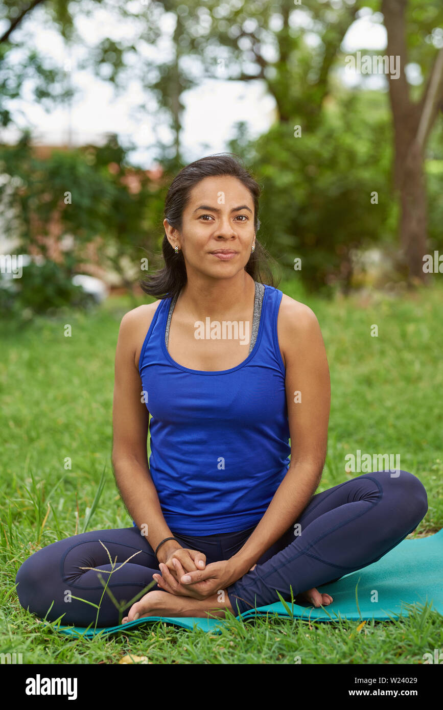 Uno stile di vita sano tema. Latina donna sedersi sul materassino yoga nel parco sullo sfondo di erba Foto Stock