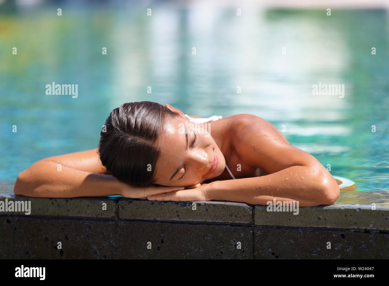 Donna rilassante a prendere il sole in piscina infinity a health spa Retreat. Lussuoso cura del corpo coccole serena giovani asiatici lady godendo sun tempo presso l'hotel e i suoi servizi. Tranquillità e comfort. Foto Stock