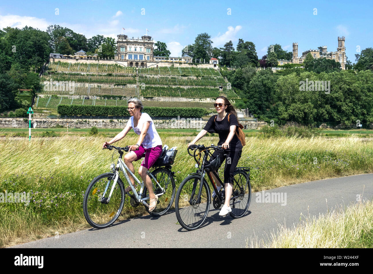 Due donne, ciclisti in bicicletta lungo il fiume Elba bike Dresda, Lignerschloss Castello Eckberg, Germania ciclismo campagna Europa Foto Stock