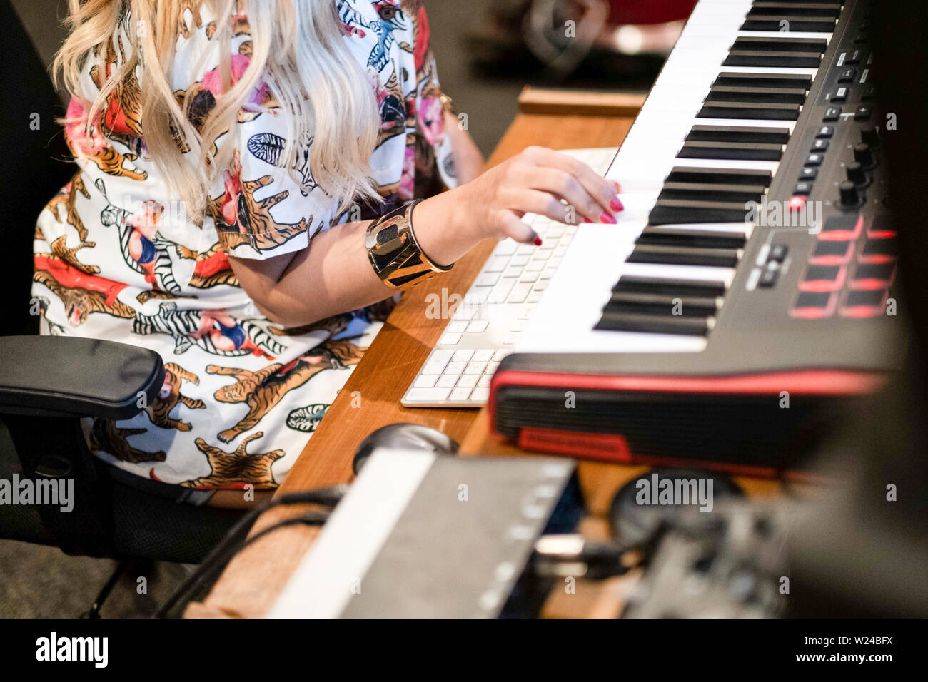 Musicista femmina lavorando in un moderno music studio di registrazione. giocando sulla tastiera e lavorando con una musica di modifica di un software per la registrazione su un grande schermo Foto Stock