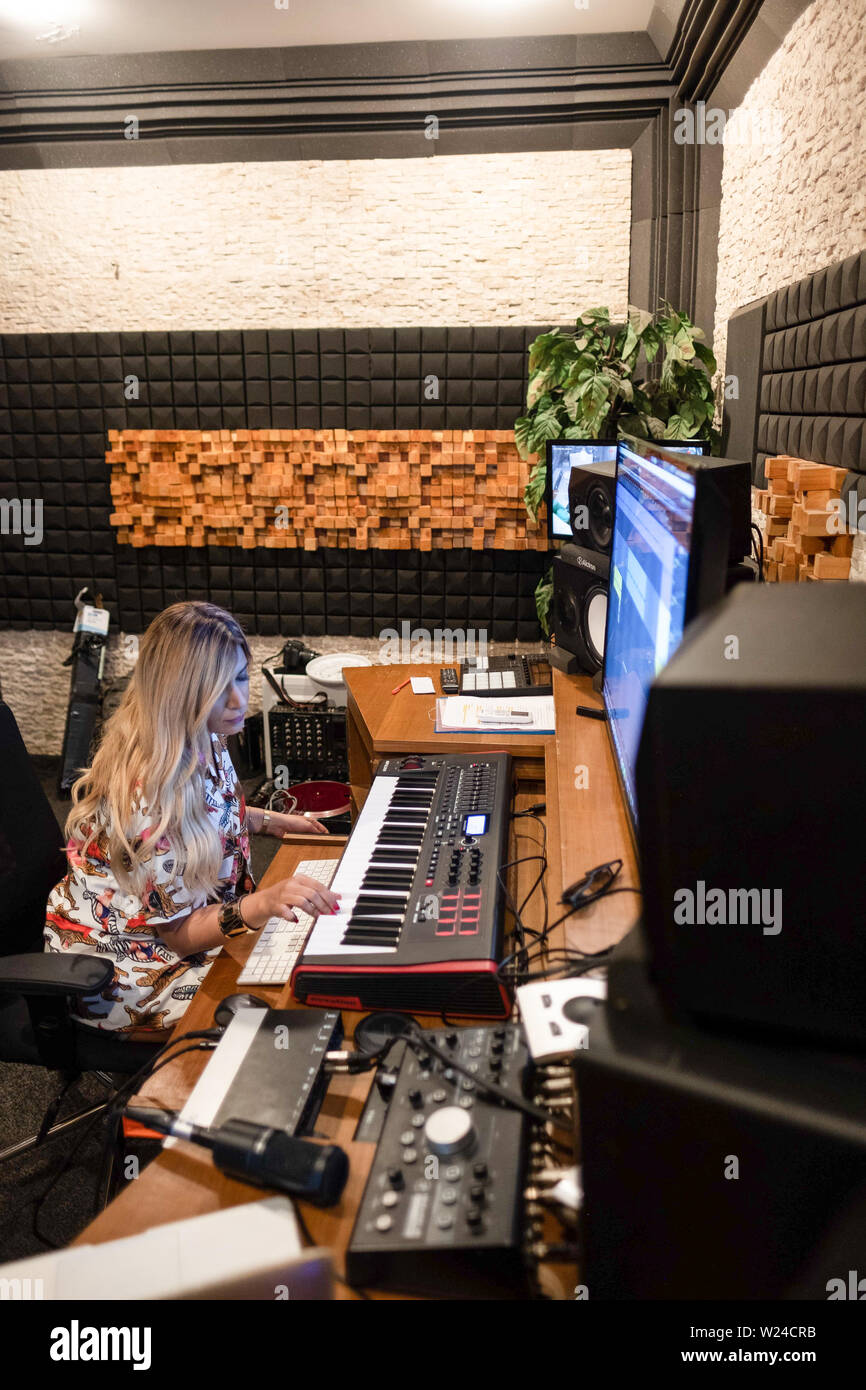 Musicista femmina lavorando in un moderno music studio di registrazione. giocando sulla tastiera e lavorando con una musica di modifica di un software per la registrazione su un grande schermo Foto Stock