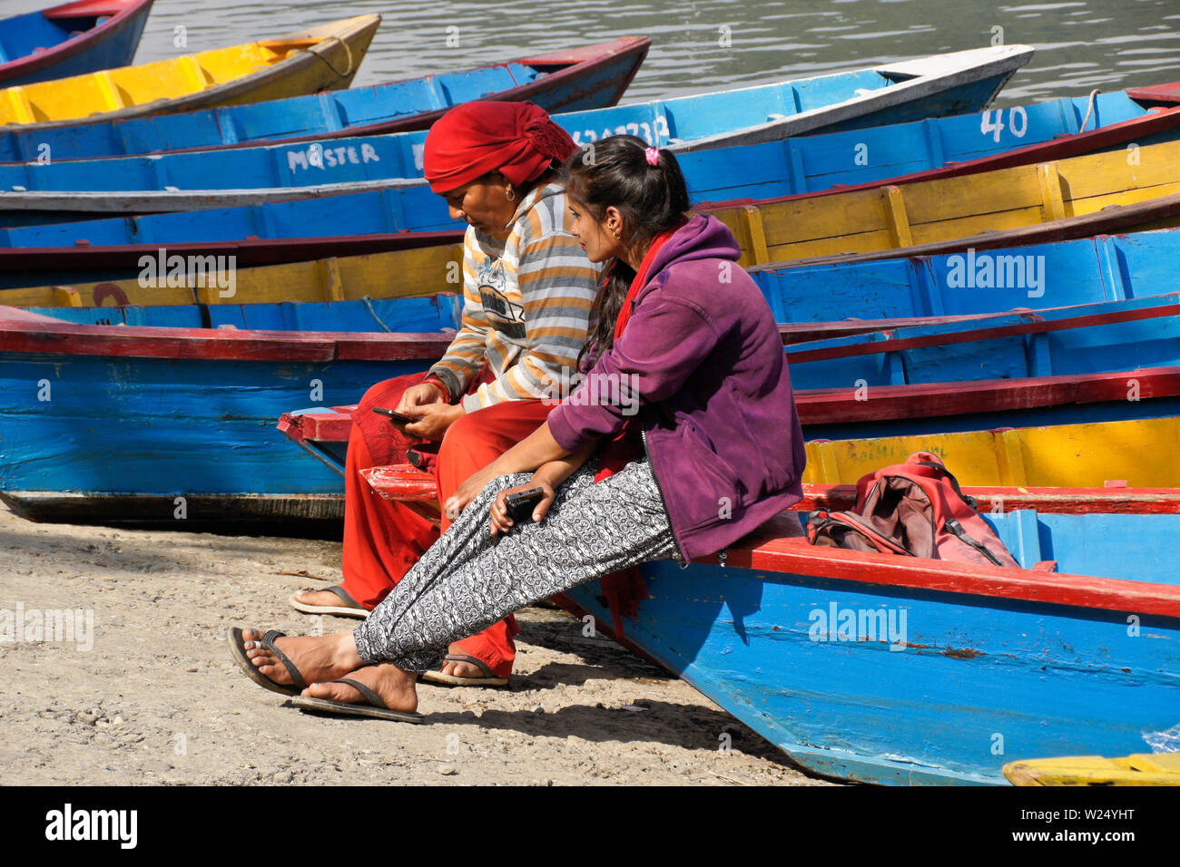 Le donne in attesa per i clienti di noleggiare colorate barche di legno a crociera sul Begnas Tal (lago Begnas) vicino a Pokhara, Nepal Foto Stock