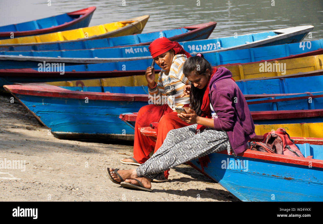 Le donne in attesa per i clienti di noleggiare colorate barche di legno a crociera sul Begnas Tal (lago Begnas) vicino a Pokhara, Nepal Foto Stock
