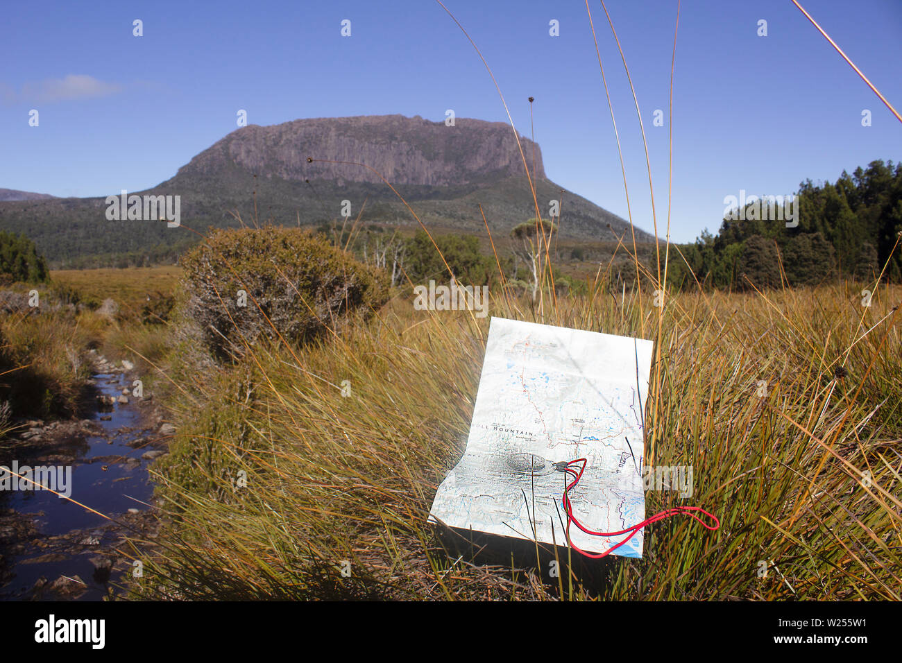 Una mappa e una bussola su un piano buttongrass nella parte anteriore di una scarpata rocciosa su Tasmania Australia Overland Track in autunno sotto un cielo blu chiaro Foto Stock