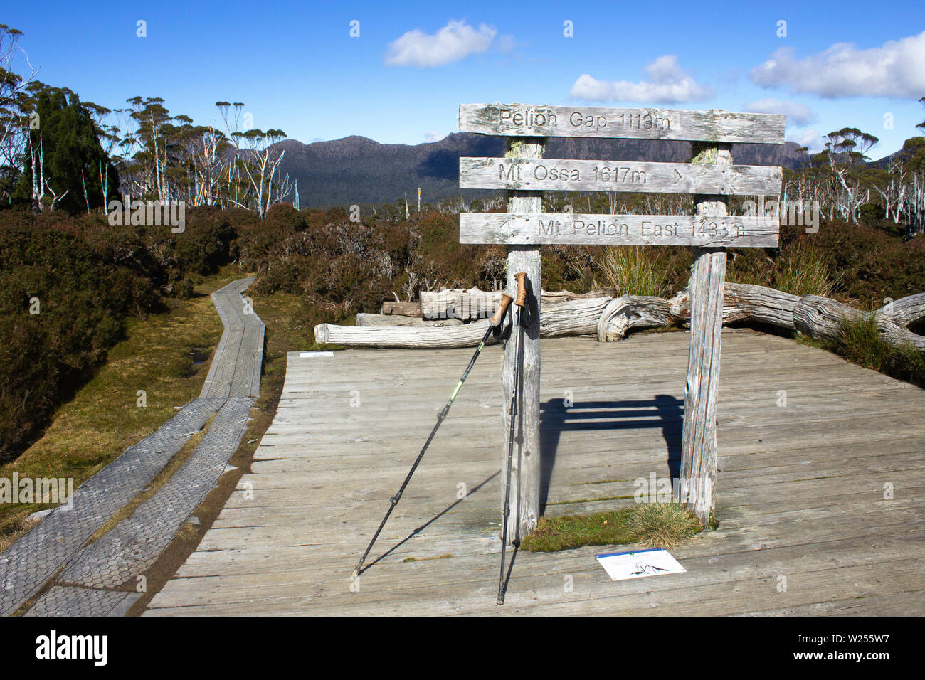 Escursionismo poli appoggiarsi contro un segno a lato le vie off Tasmania, la Overland Track, mentre la principale via corre attraverso l'immagine. Foto Stock