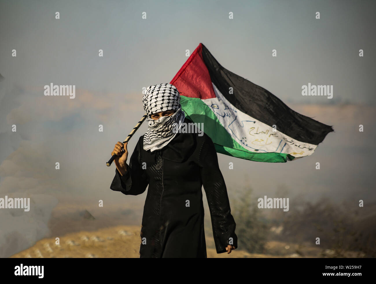 La striscia di Gaza, la Palestina. 05 Luglio, 2019. Una donna Palestinese porta la bandiera palestinese con in una valanga di gas lacrimogeni durante una manifestazione per chiedere la fine dell'assedio imposto alla striscia di Gaza nel sud della striscia di Gaza. Credito: SOPA Immagini limitata/Alamy Live News Foto Stock