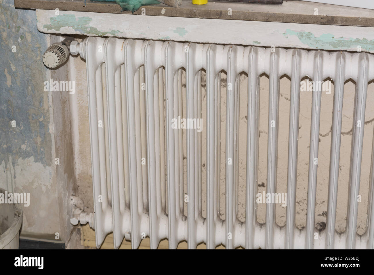 Vecchio radiatore in metallo o tubo alettato riscaldatore su un bianco muro di pietra Foto Stock