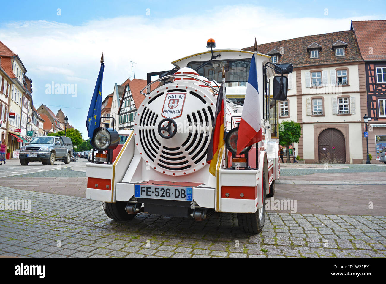 Tour di confine con il bianco touristic mini treno auto sagomata con il tedesco e il francese bandiera davanti, in piedi sulla piazza del mercato a Wissembourg Francia Foto Stock