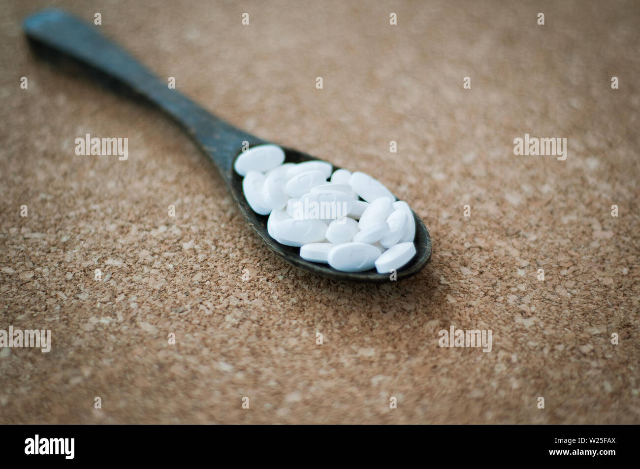 Bianco pillole di prodotti farmaceutici e medicinali in il cucchiaio di legno su un sughero marrone dello sfondo. Valentines, cuore, malati, salute e il concetto di guarigione. Foto Stock